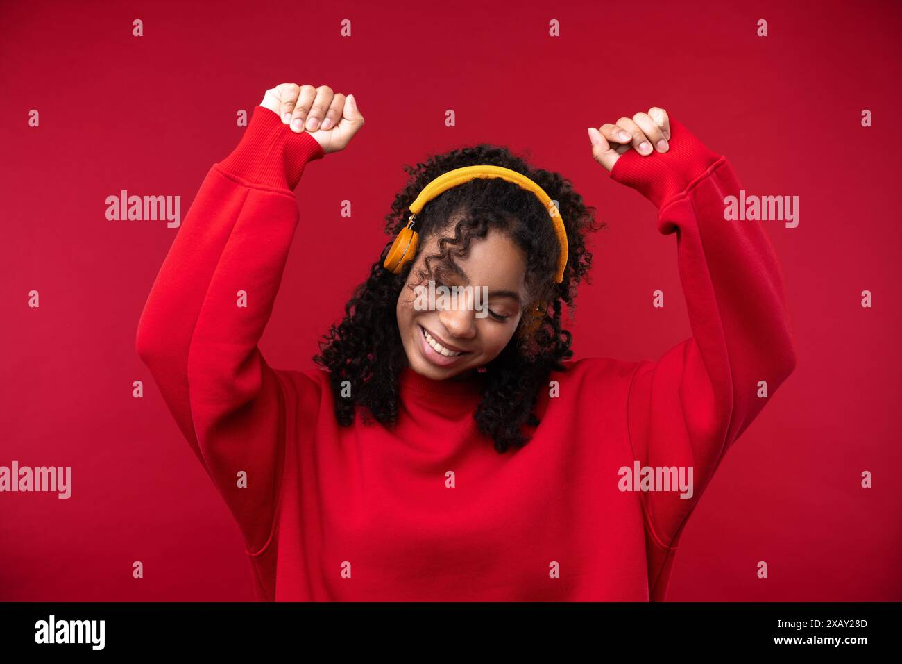 Porträt eines jungen Mädchens, das vor rotem Hintergrund in die Kamera lächelt. Glückliche schwarze Frau, die ihr natürliches Haar umschließt. Stockfoto