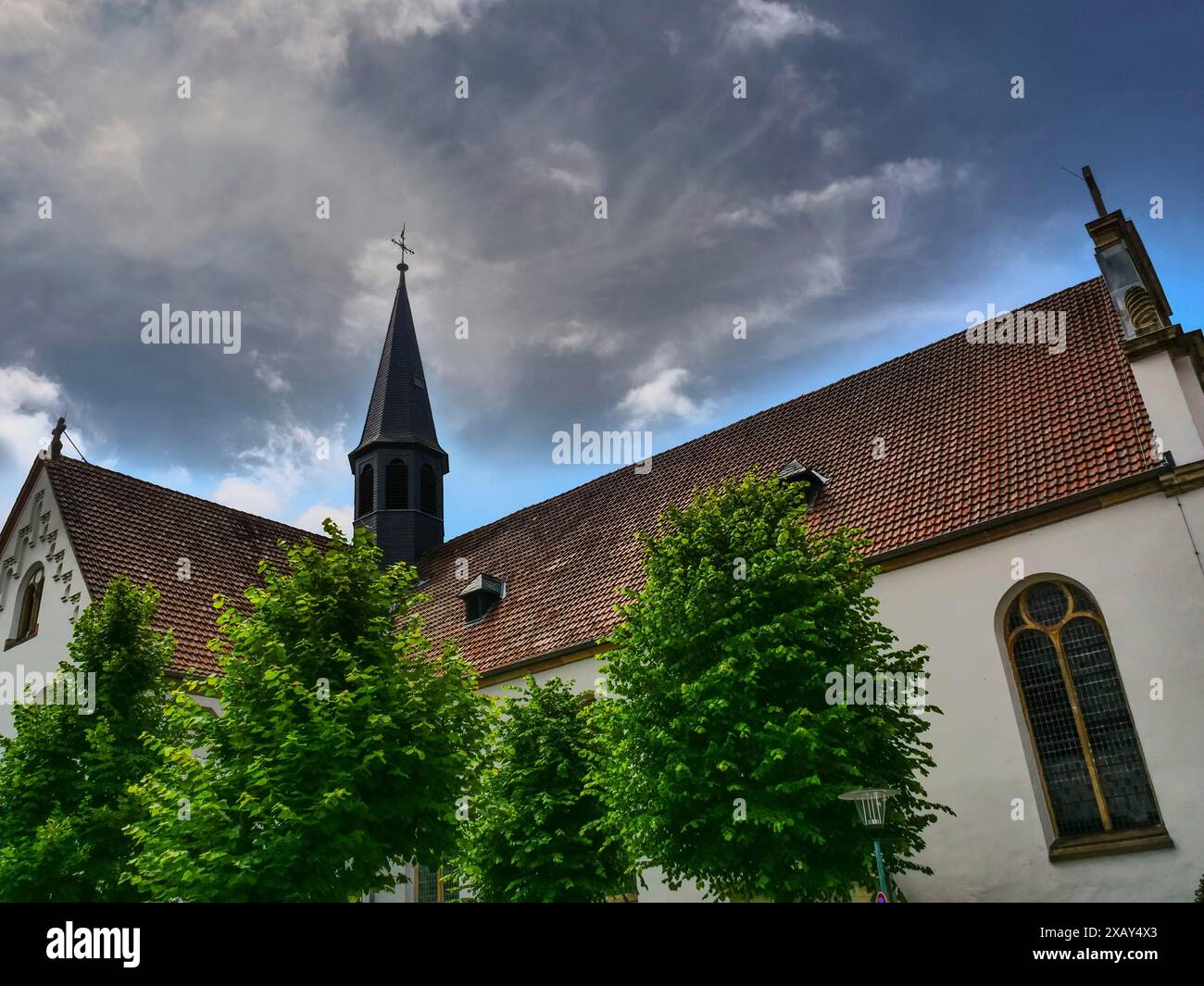 Kirche mit rotem Ziegeldach und dunklem Turm, grünen Bäumen und einem dramatischen Himmel im Vordergrund, Steinfurt, Nordrhein-Westfalen, Deutschland Stockfoto