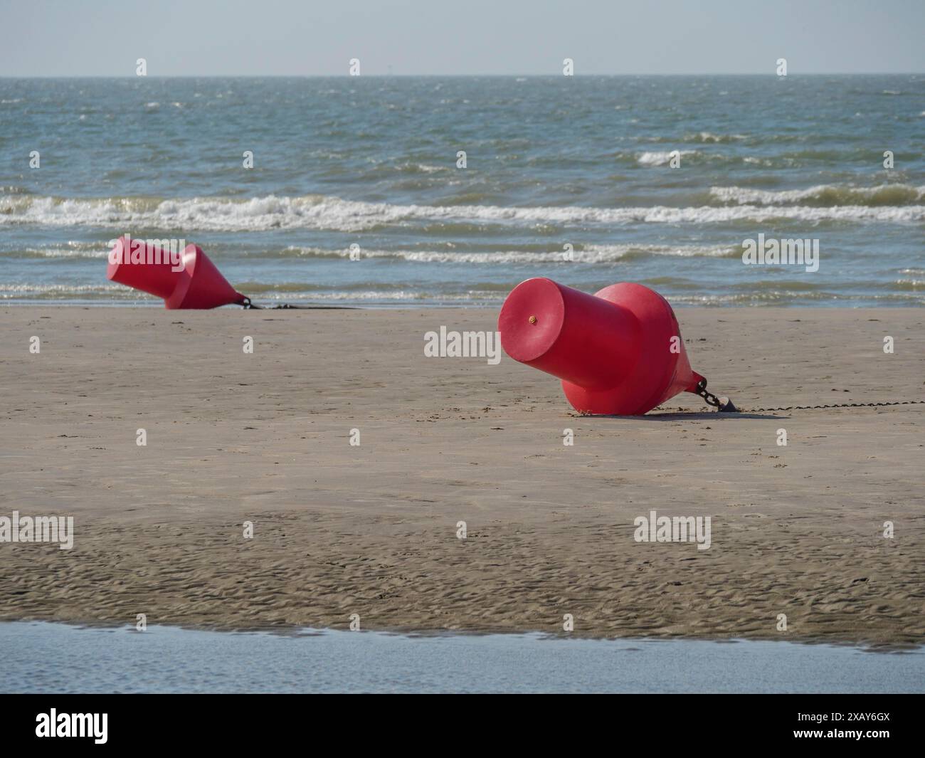 Zwei rote Bojen liegen am Strand in der Nähe des Wassers und der Wellen eines ruhigen Meeres, de haan, belgien Stockfoto