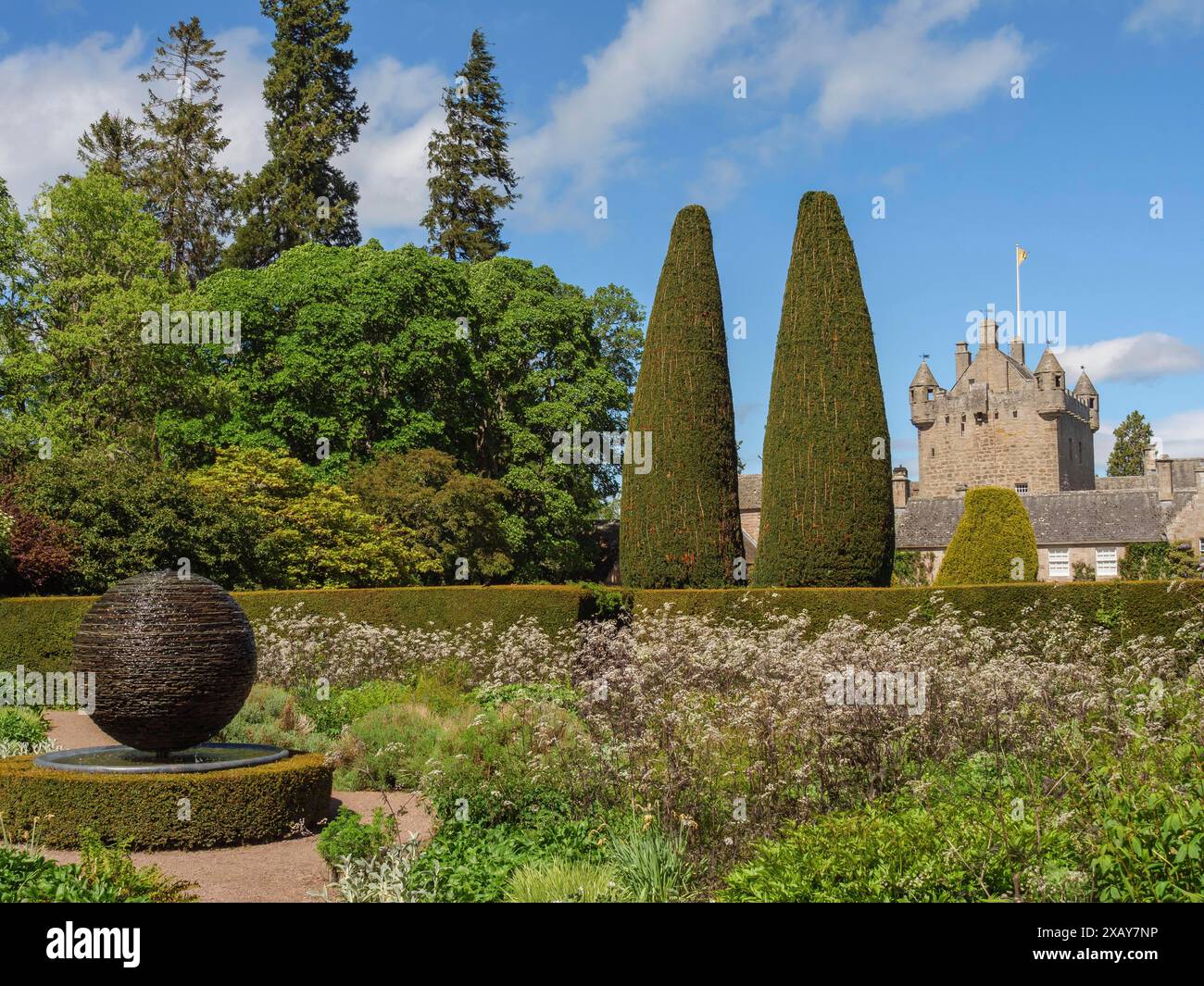 Grüner Garten mit Hecken, Pflanzen und einer Skulptur, im Hintergrund eine Steinburg unter blauem Himmel, inverness, Schottland, Großbritannien Stockfoto