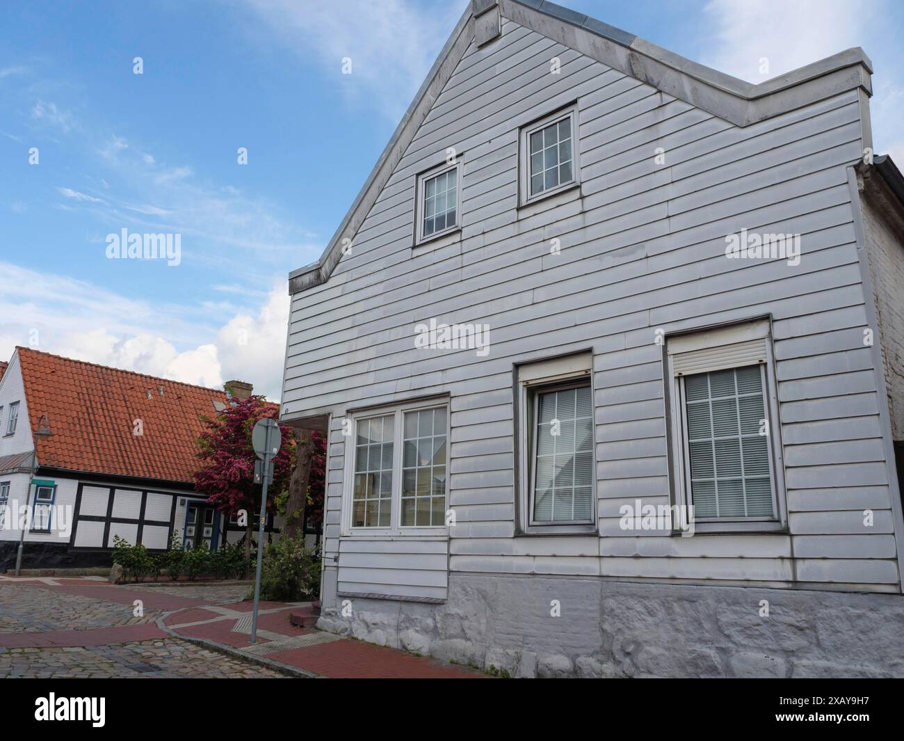 Ein weißes historisches Holzhaus steht auf einer Kopfsteinpflasterstraße unter blauem Himmel in Eckernförde, Schleswig-Holstein, Deutschland Stockfoto