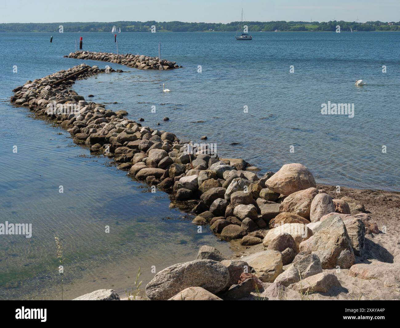 Ein Steinpfeiler ragt in das ruhige Wasser eines Sees unter klarem blauem Himmel, Flensburg, Schleswig-Holstein, Deutschland Stockfoto