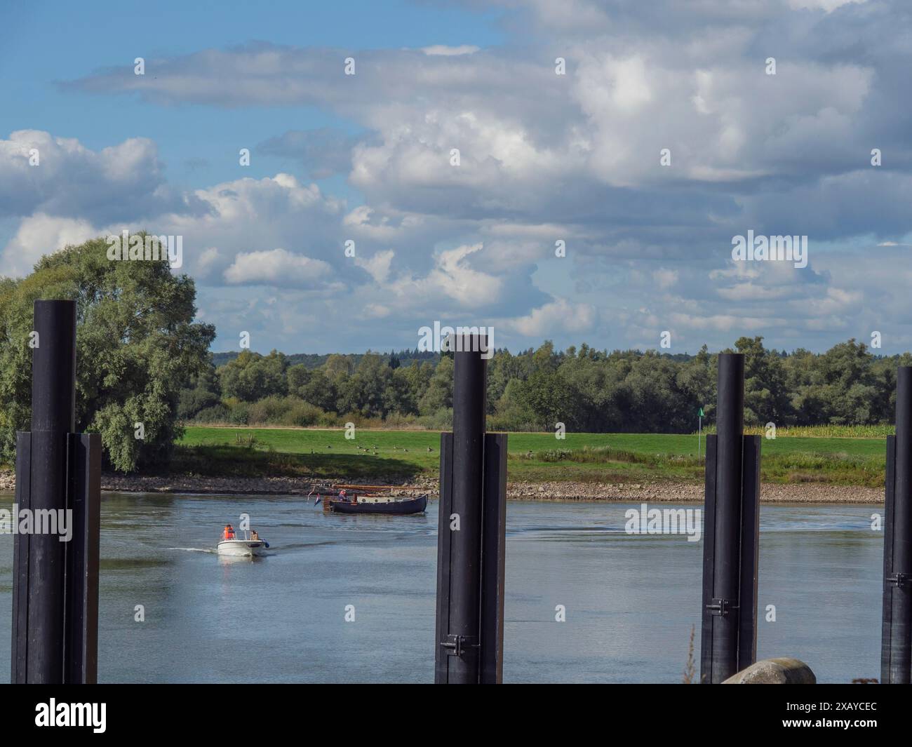 Ein Boot und mehrere Pfosten in einem ruhigen Fluss, umgeben von grünem Land und Wolken, Doesburg, Niederlande Stockfoto