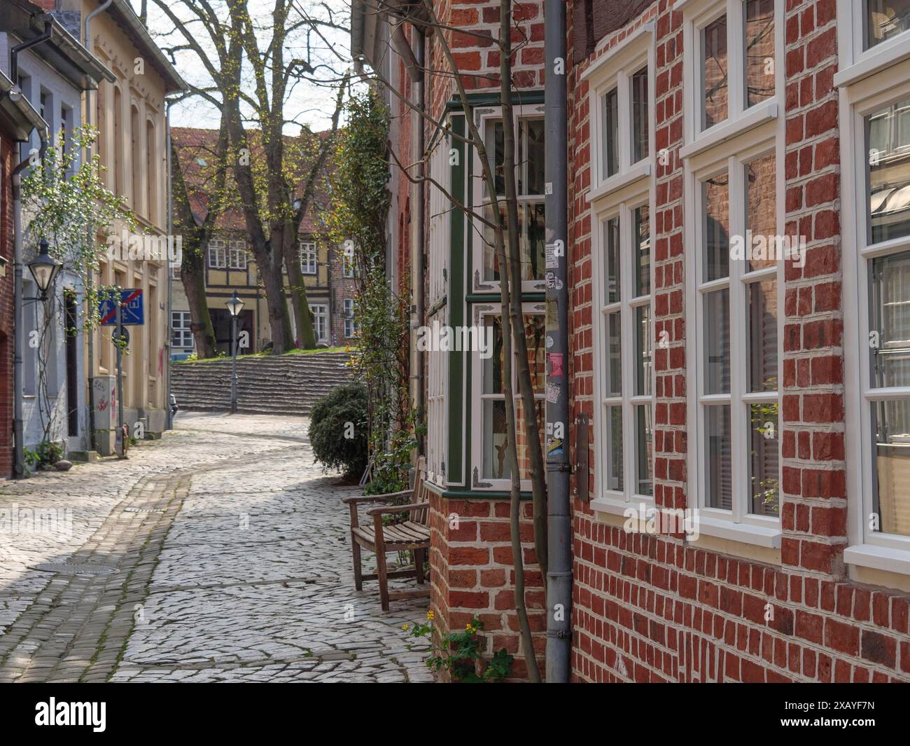 Idyllische, gepflasterte Straße gesäumt von historischen Gebäuden mit roten Backsteinmauern, Bäumen im Hintergrund, lüneburg, deutschland Stockfoto