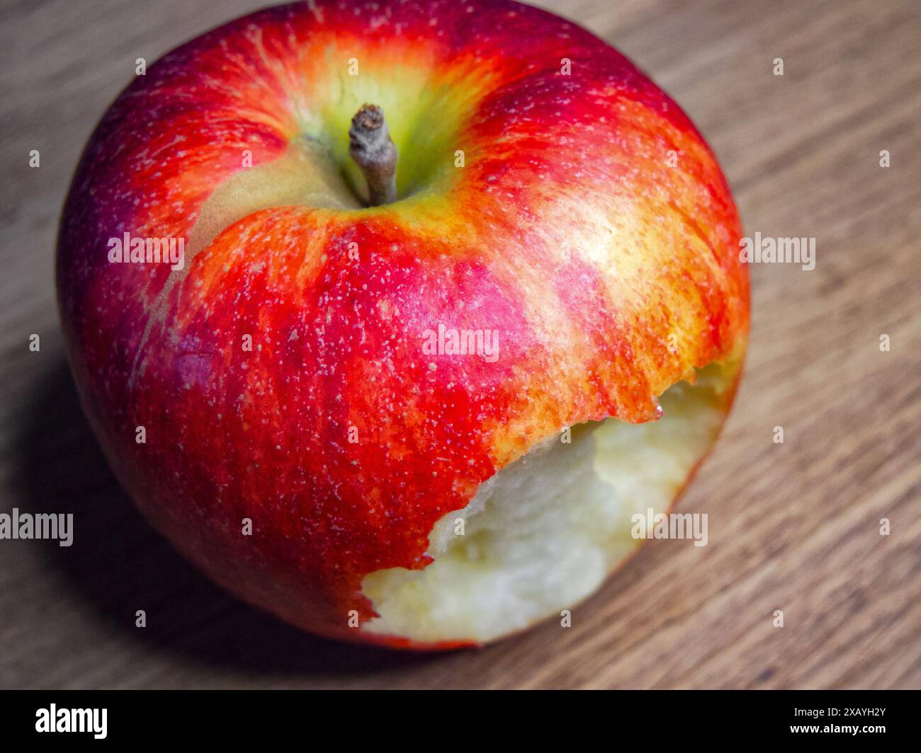 Halb Gegessen Apfel. Ein leuchtender roter Apfel, teilweise gegessen, vor hölzernem Hintergrund, geeignet für Ernährung und Ernährung. Stockfoto