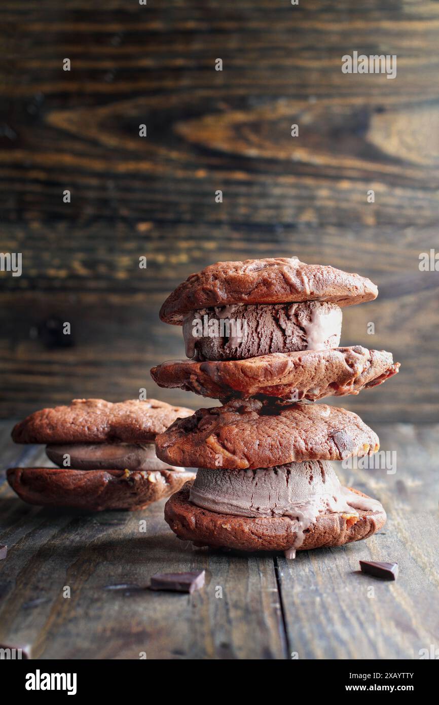 Schokoladen-Schokoladen-Eis-Cookie-Sandwiches, die mit Stückchen Schokoladenbonbons zubereitet und mit Milchschokolade-Eis über einem dunklen rustikalen Hintergrund gefüllt sind Stockfoto