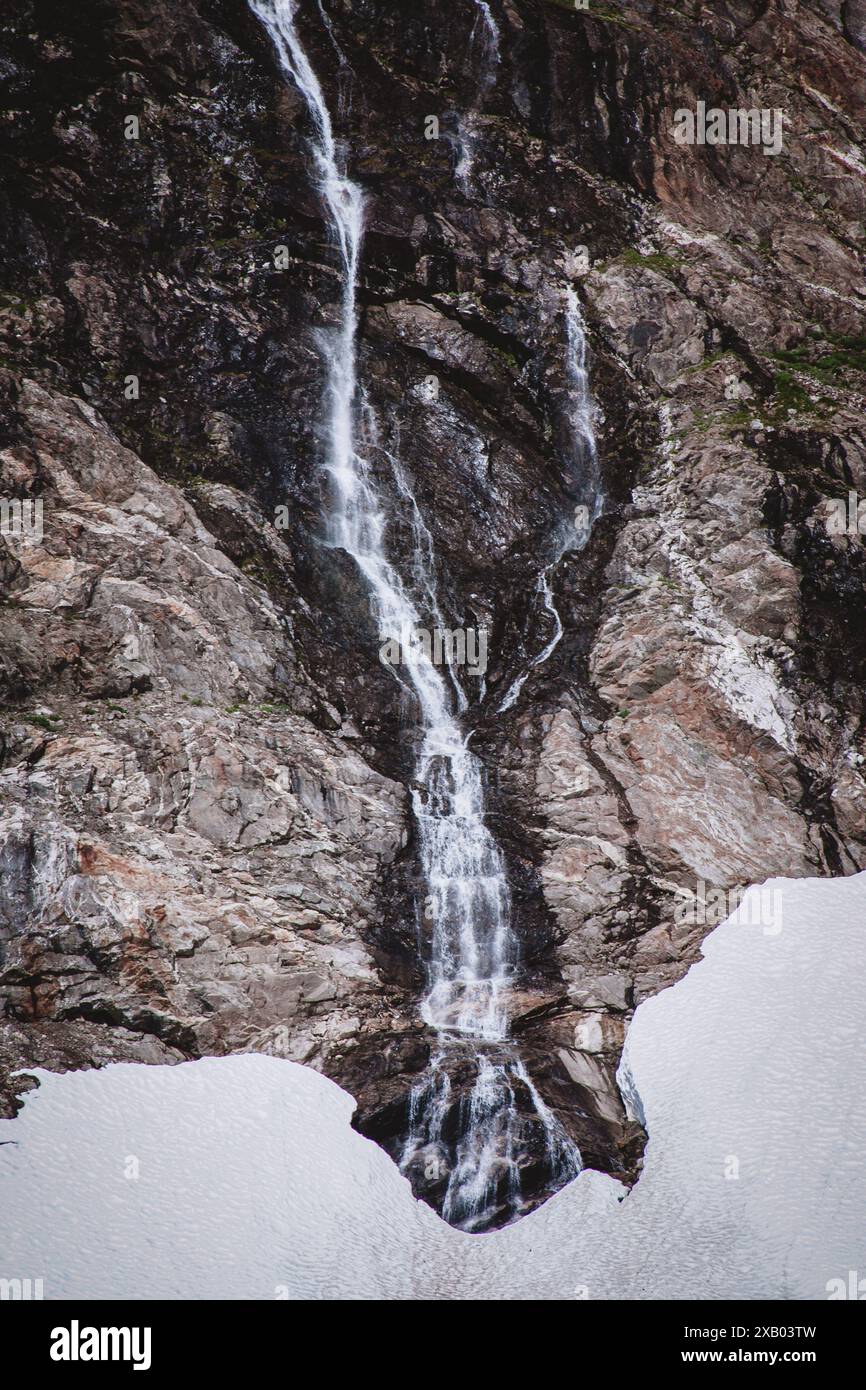 Eine atemberaubende Nahaufnahme eines Wasserfalls, der die zerklüfteten, eiskalten Hänge eines alaskischen Gletschers hinunterstürzt. Die kontrastierenden Texturen und die natürliche Schönheit machen dies aus Stockfoto