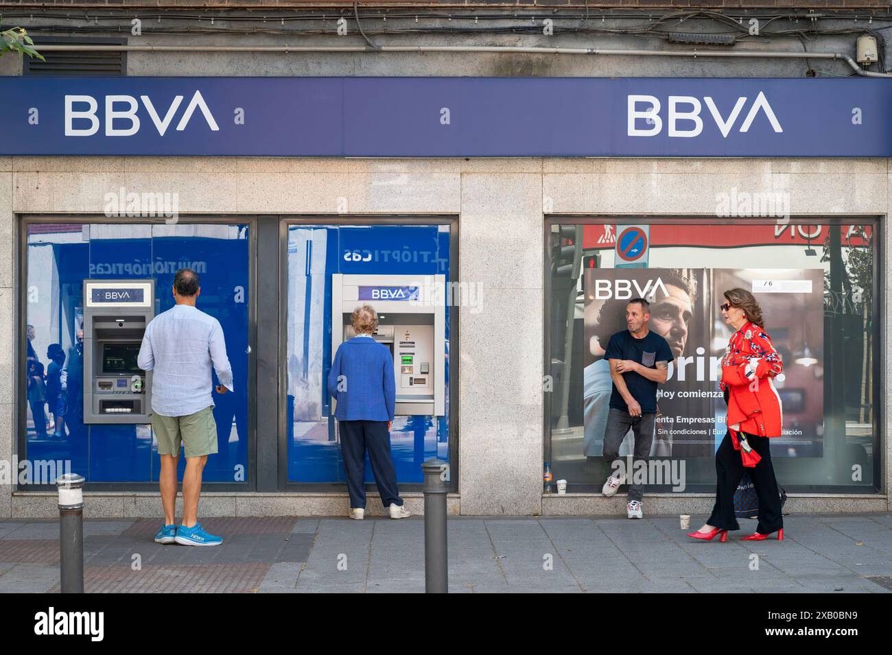 Ein Kunde hebt Geld ab, während andere an einem Geldautomaten bei der spanischen multinationalen Bank Banco Bilbao Vizcaya Argentaria SA (BBVA) in Spanien anstehen. Stockfoto