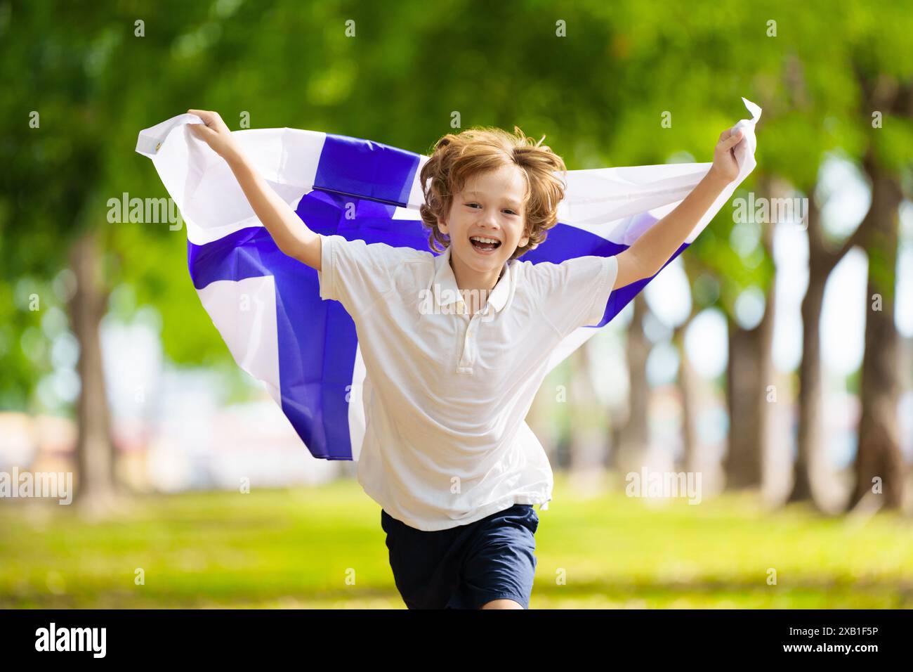 Kind läuft mit Finnlandflagge. Kleiner finnischer Junge, der dem Fußballteam zujubelt. Suomi-Fans auf dem Fußballfeld beobachten das Teamspiel. Stockfoto