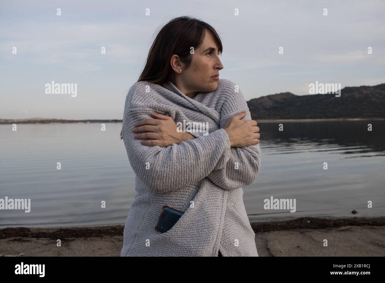 Junge Frau, die an einem kalten, windigen Strand steht, in eine warme Jacke gewickelt. Stockfoto