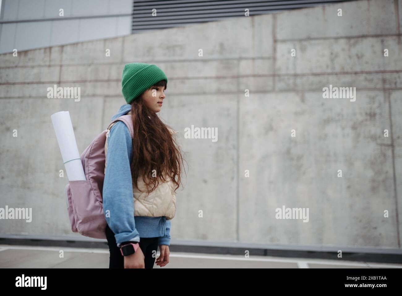 Außenporträt eines traurigen jungen Mädchens mit Mütze und Rucksack. Ein Mädchen mit langen Haaren geht zur Schule und fühlt sich ängstlich. Stockfoto