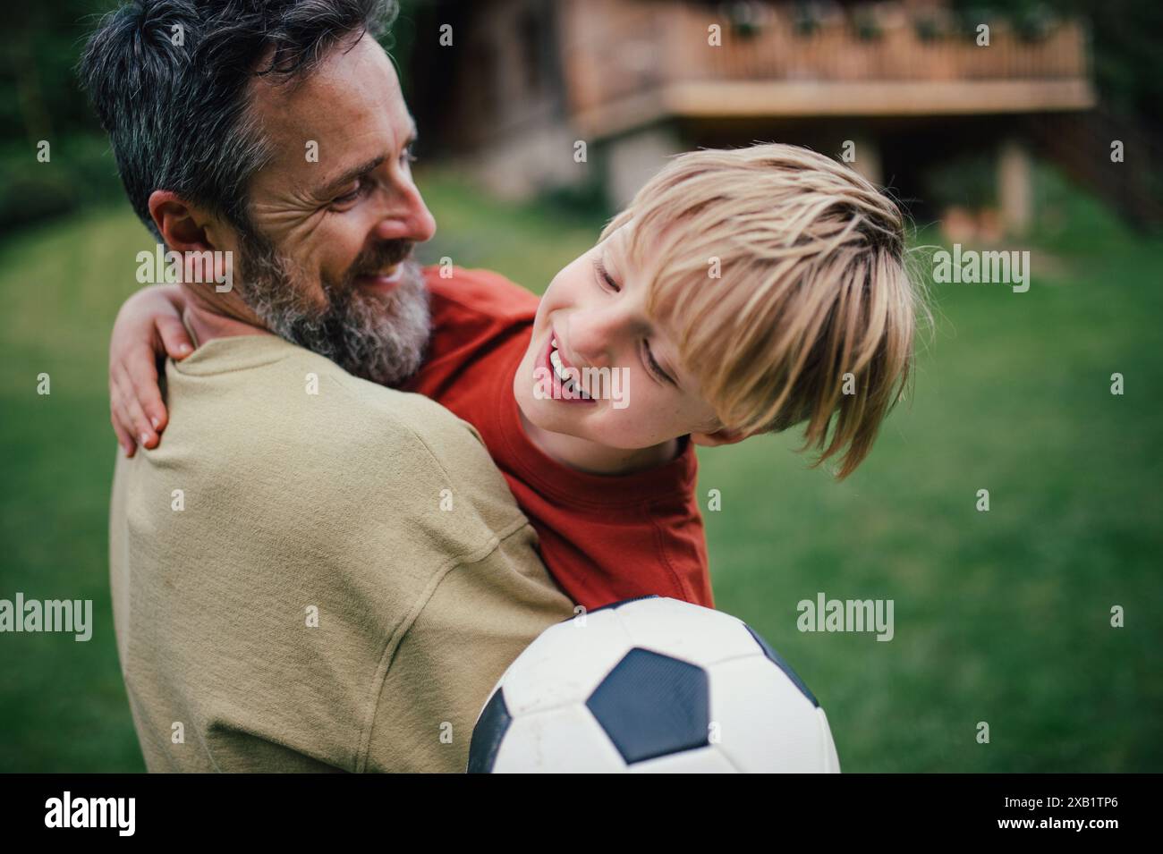Dad nimmt den jungen Sohn an, läuft und feiert den Sieg nach dem Tor. Fußball spielen auf dem Rasen vor ihrem Haus. Vaterschaft und Vatertag. Stockfoto