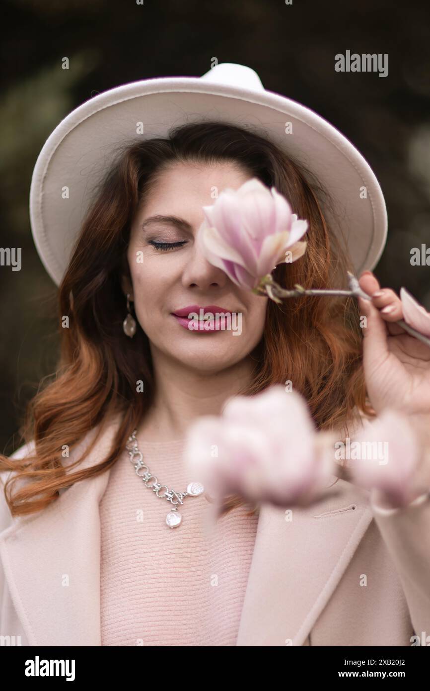 Die Frau hält Magnolienblüten, umgeben von blühenden Bäumen. Im Frühling mit natürlicher Schönheit und saisonalem Wandel Stockfoto