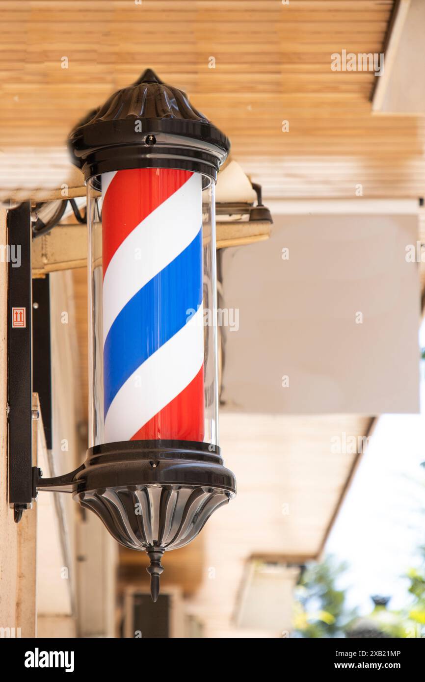 Ein klassisches Friseurpfosten-Schild mit roten, weißen und blauen Streifen vor einem Friseurladen in einem Stadtgebiet. Stockfoto