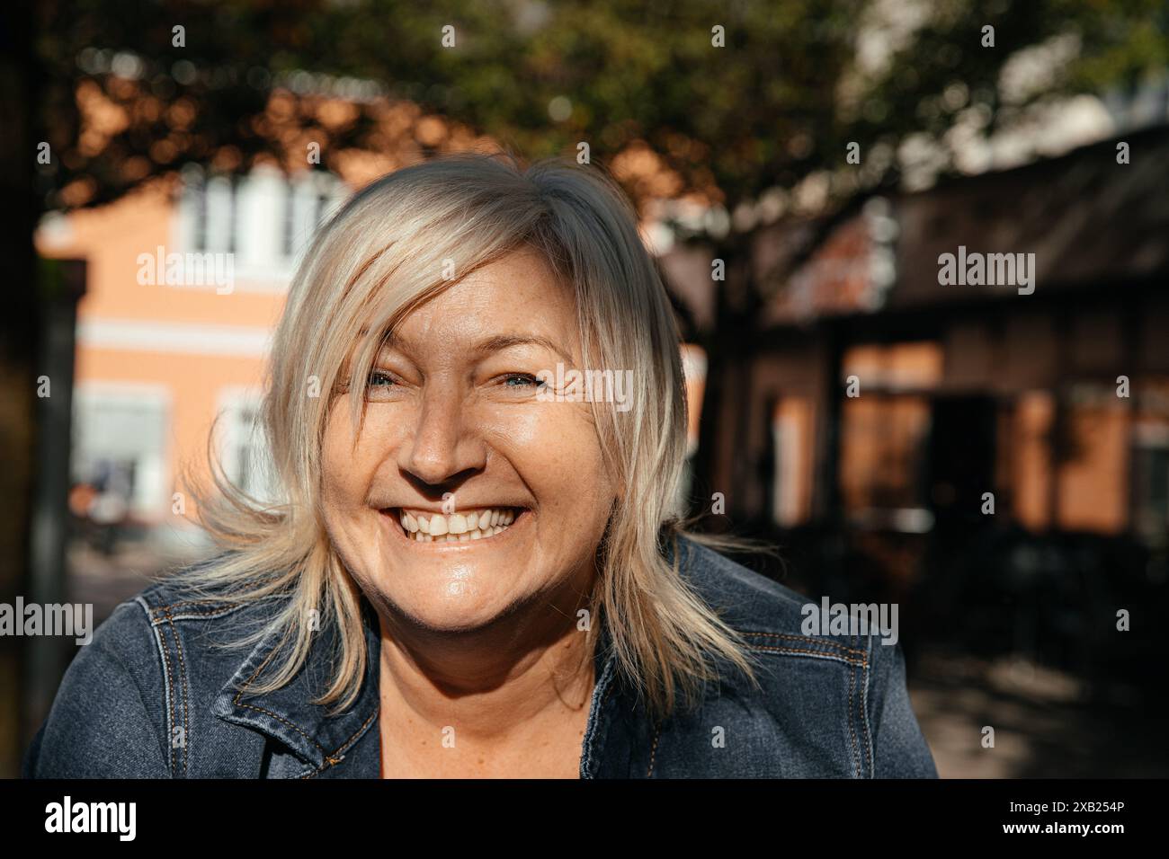 Eine ältere Frau mit blonden Haaren und einem hellen Lächeln, die Sonnenschein genießt Stockfoto