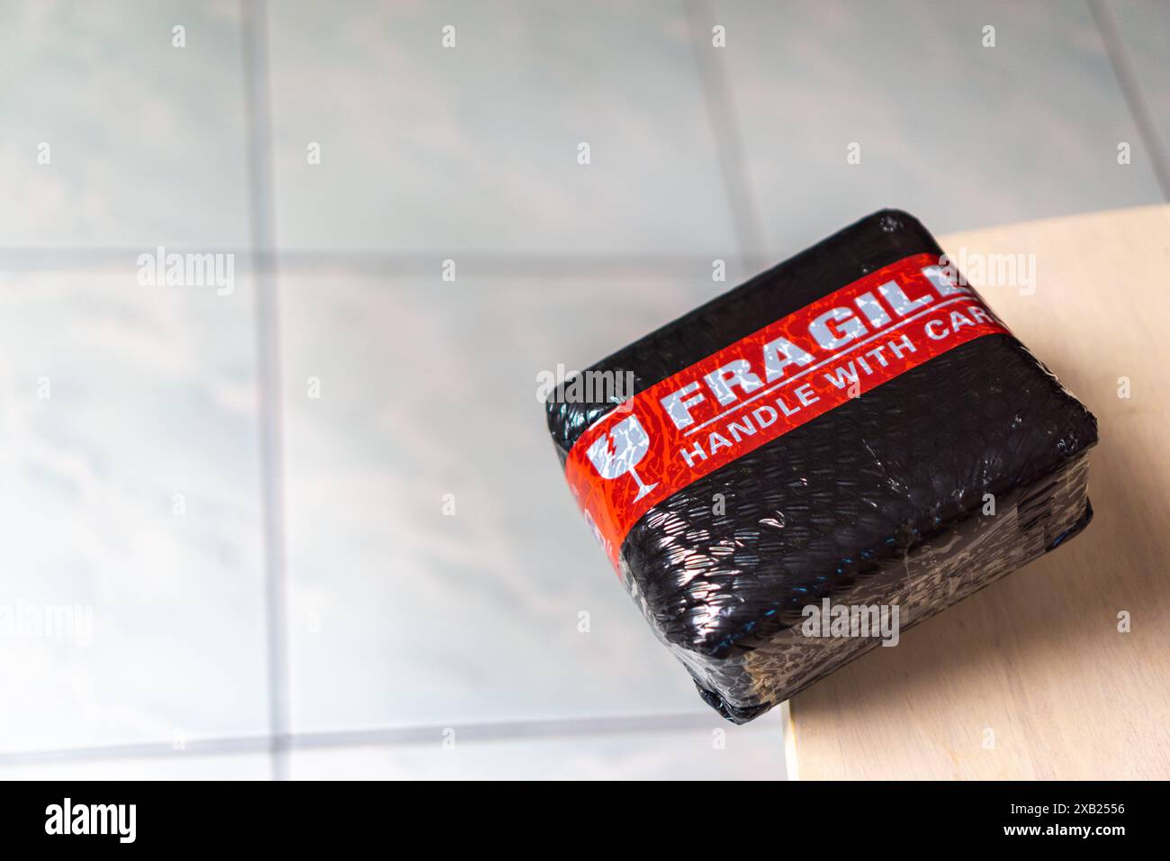 Lieferung nach Hause, ein Paket mit einem zerbrechlichen Griff mit Pflegeaufkleber, das fast auf eine Seite eines Tisches fällt Stockfoto