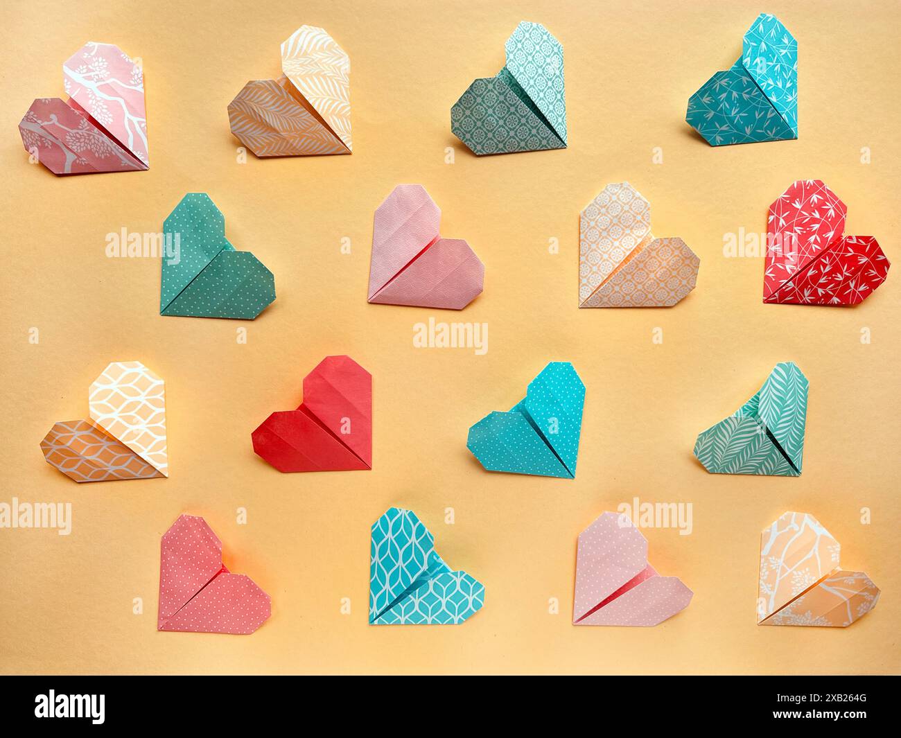 Bunte Origami-Papier-Herzen in symmetrischen Mustern auf beigefarbenem Hintergrund angeordnet Stockfoto