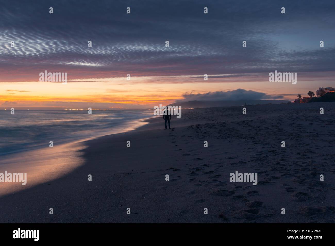 Am Atlanterra Beach, der von einem dramatischen Abendhimmel in Cadiz überschattet wird, steht eine einzelne, nicht erkennbare Silhouette. Stockfoto