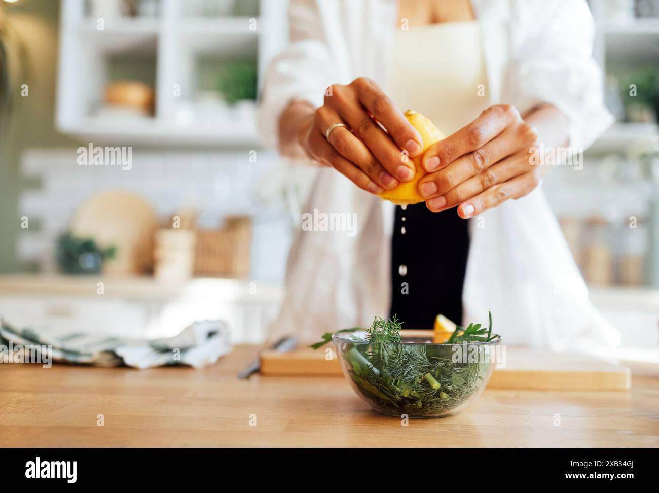 Eine weibliche, gepflegte Hände mit einer gepflegten Maniküre, die Zitronensaft in eine Glasschale mit Salat drückt. Gesunde Ernährung. Frischer grüner Salat mit Rucola Stockfoto