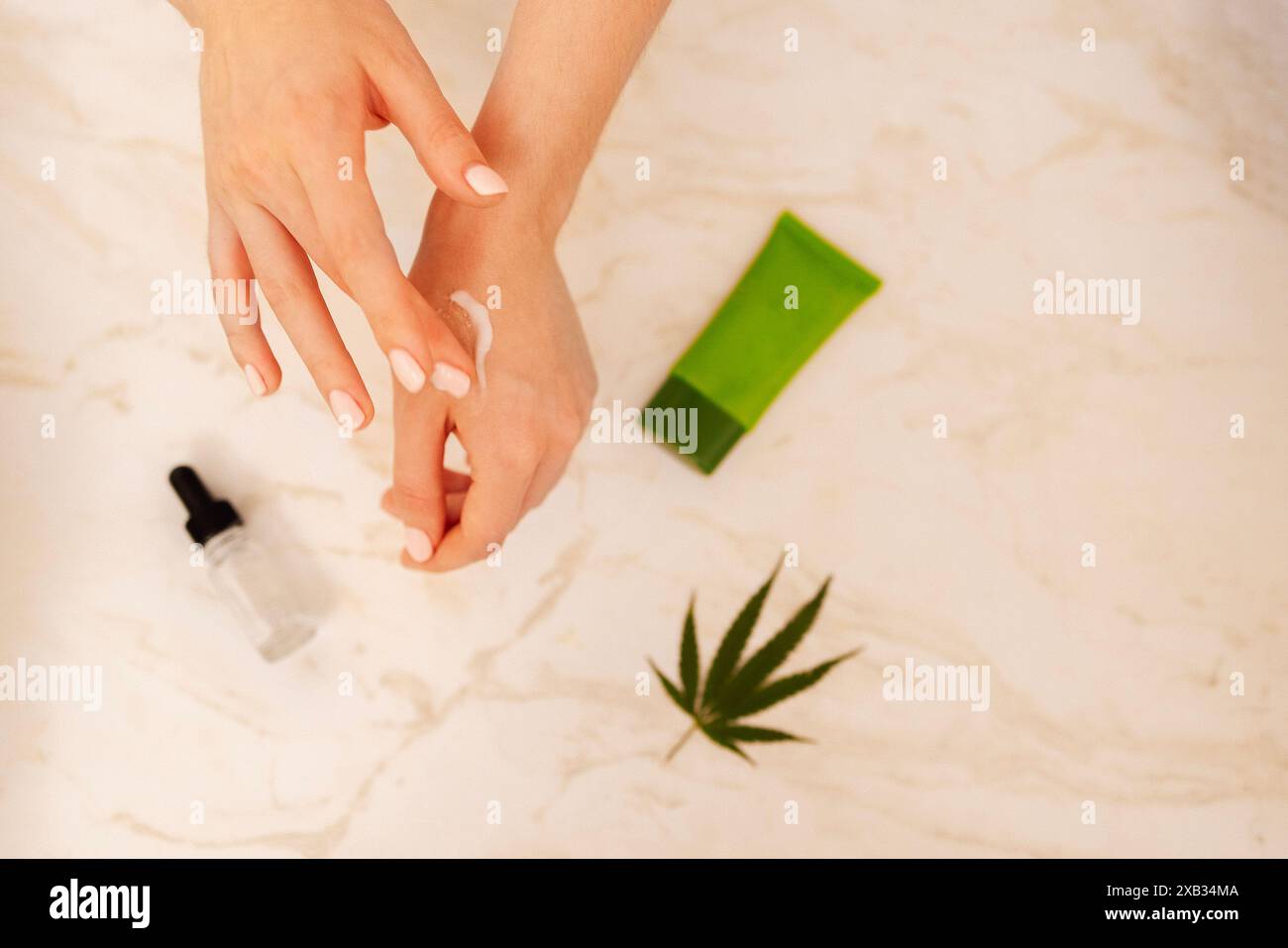 Nahaufnahme der gepflegten Hände einer jungen Frau mit einer Feuchtigkeitscreme aus Cannabis. Handhautpflege. Ein Modell einer Röhre, eine Flasche Serum Stockfoto