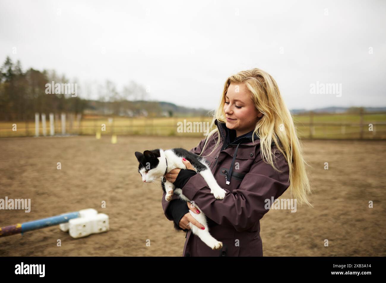 Blonde junge Frau, die Katze in Armen hält, während sie auf der Ranch gegen den Himmel steht Stockfoto