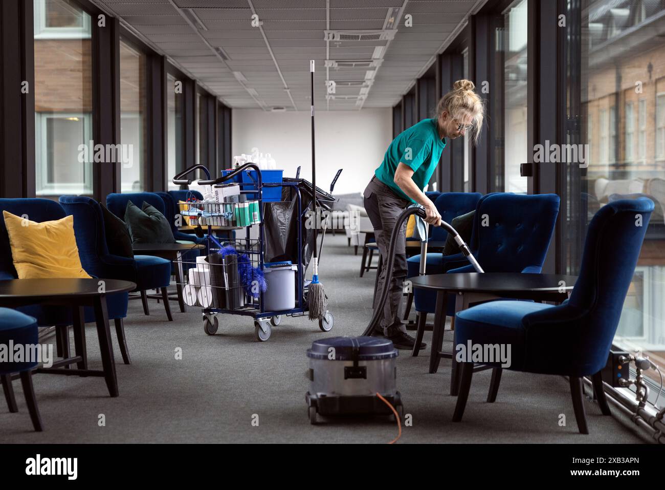 Volle Länge der Reifen weiblichen Hausmeister-Lobby mit Staubsauger Stockfoto