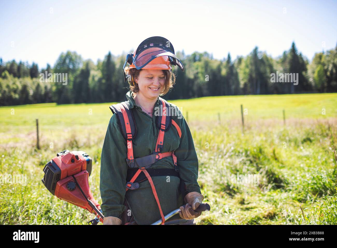 Lächelnde Frau, die Arbeitskleidung trägt und Unkrautschneider im Hof hält Stockfoto