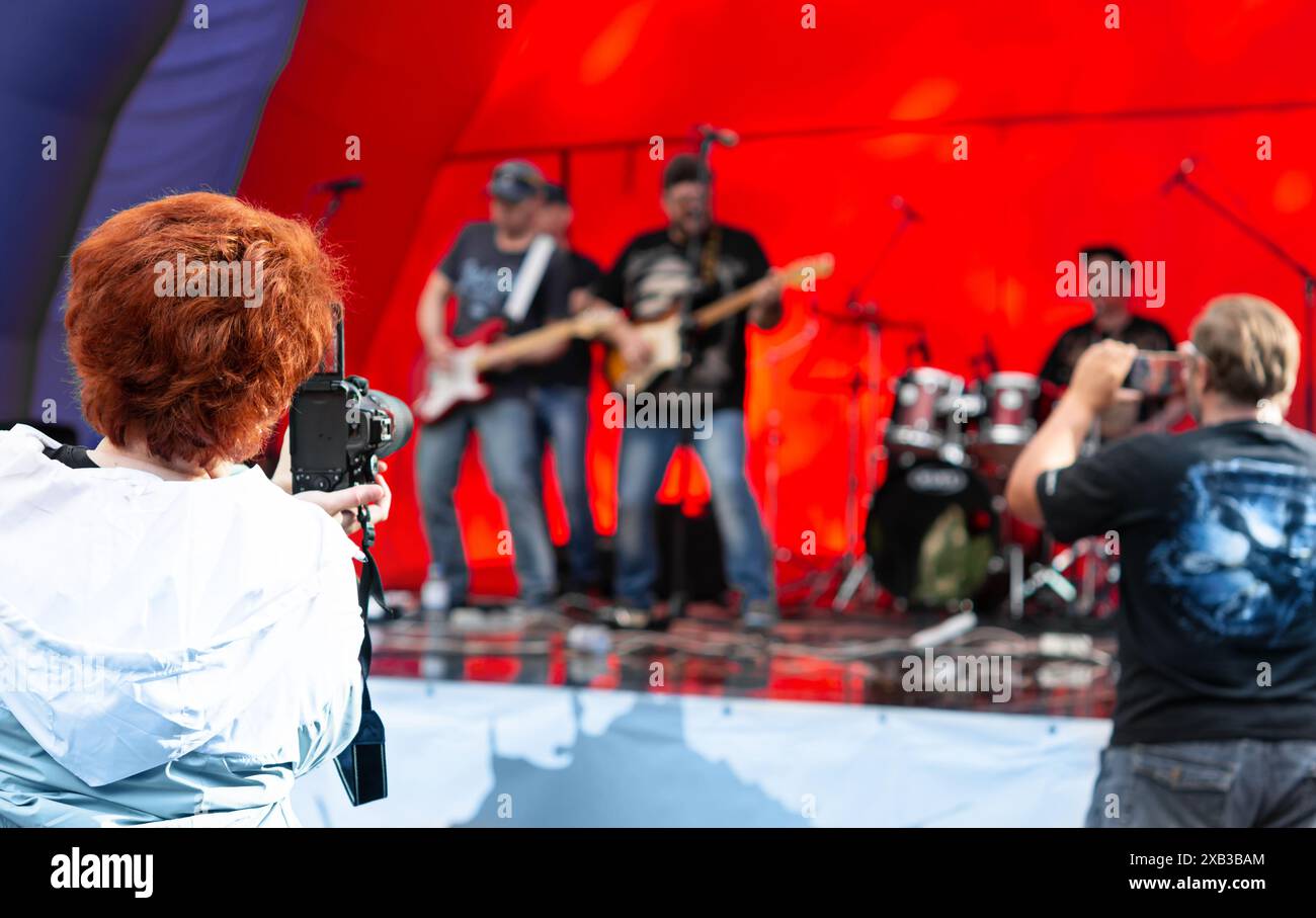Eine Frau nimmt die lebhafte Konzertatmosphäre mit einer Videokamera vor rotem Hintergrund auf und verkörpert das El Stockfoto