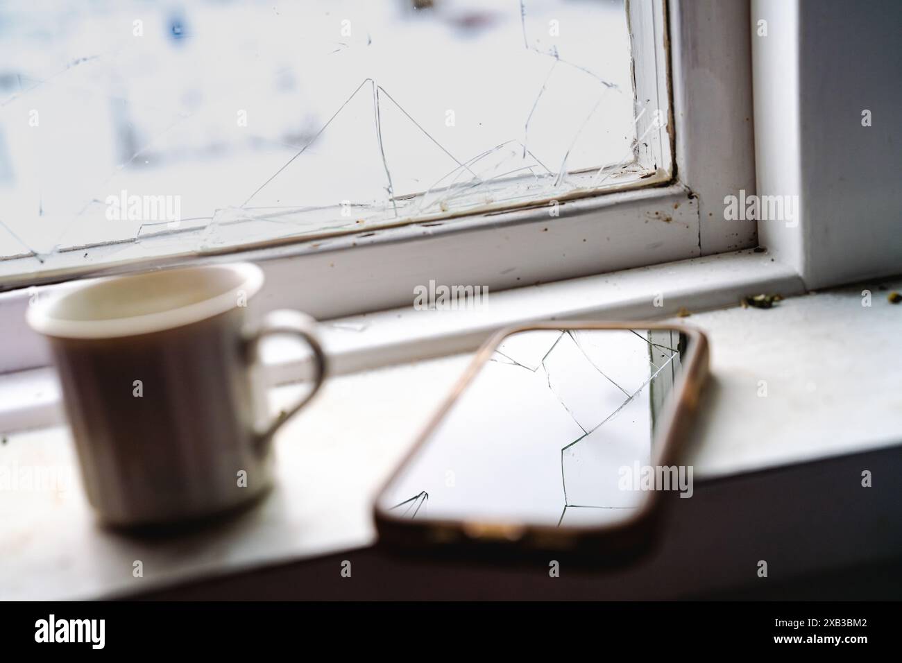 Nahaufnahme des beschädigten Smartphones und der Kaffeetasse am Fenster Stockfoto