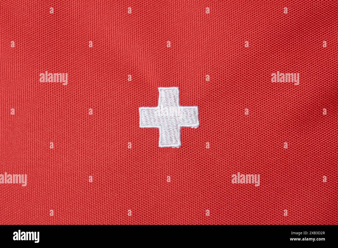 Weißes Krankenhaus plus oder medizinisches Kreuzzeichen auf rotem texturiertem Stoffoberflächenhintergrund, gestickte schweizer Nationalflagge mit Kopierraum Stockfoto