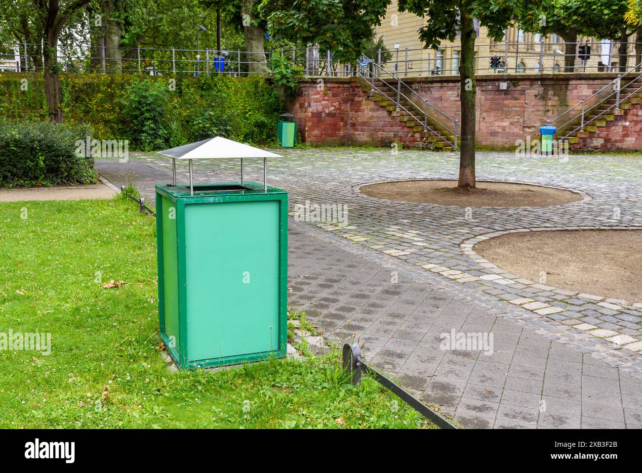 Mülltonne entlang eines einsamen Steinwegs in einem öffentlichen Park Stockfoto