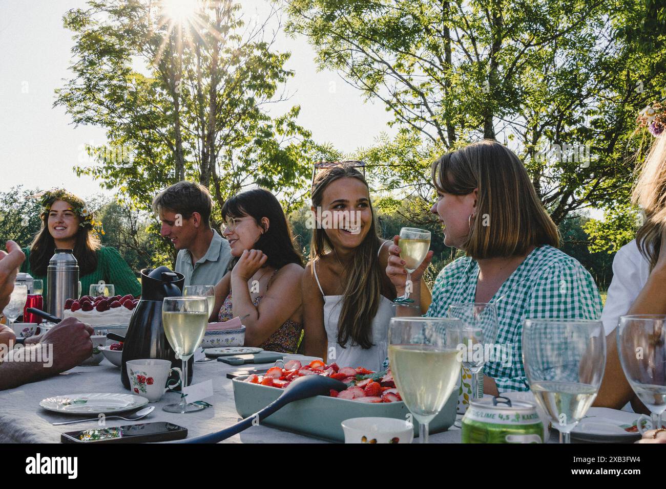 Glückliche junge Freunde sitzen am Esstisch im Hinterhof während einer Gartenparty am Wochenende Stockfoto