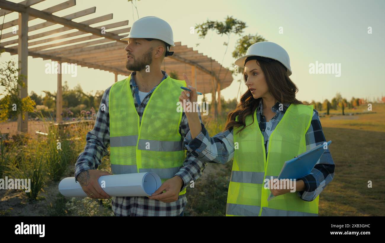 Kaukasische Kollegen Architektenpartnerschaft männlicher Mann Geschäftsmann Ingenieur halten Blueprint, der Talk erklärt weibliche Geschäftsfrau Inspektorin Frau schreibt Stockfoto