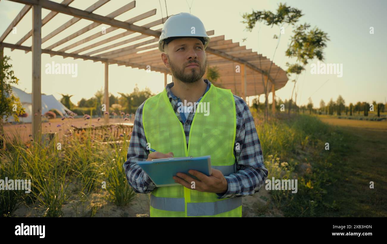 Kaukasischer männlicher Geschäftsmann Mann Guy Hardhat Uniform Ingenieur arbeitender Architekt zuversichtlicher Inspektor Schreiben Tablet Clipboard Controlling Projekt Stockfoto