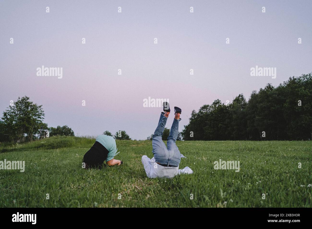 Niedriger Teil des gefallenen jungen Paares, das bei Sonnenuntergang auf Gras vor klarem Himmel rollte Stockfoto