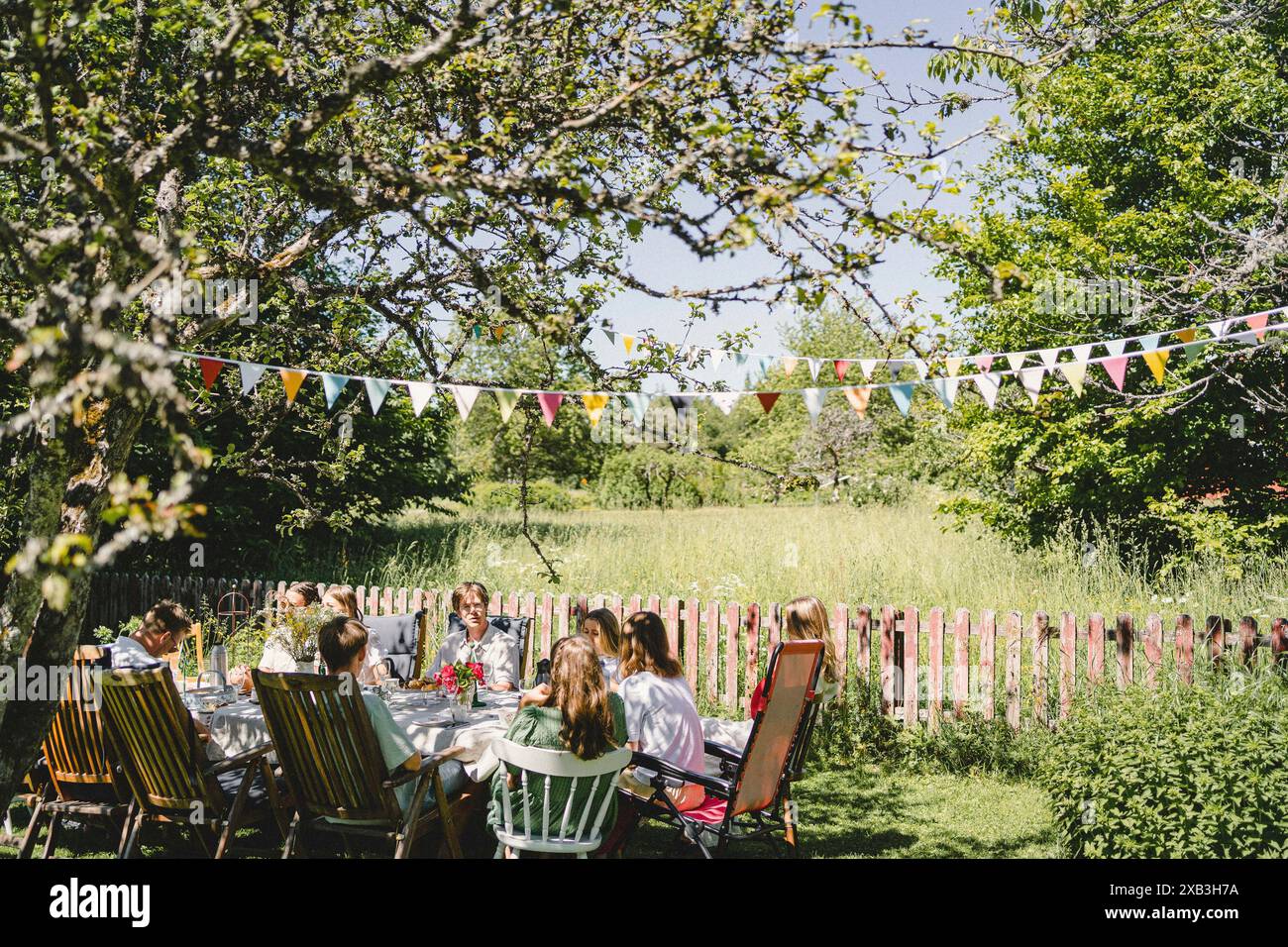 Junge Freunde, die während der Sommersonnenfeier im Hinterhof am Esstisch sitzen Stockfoto