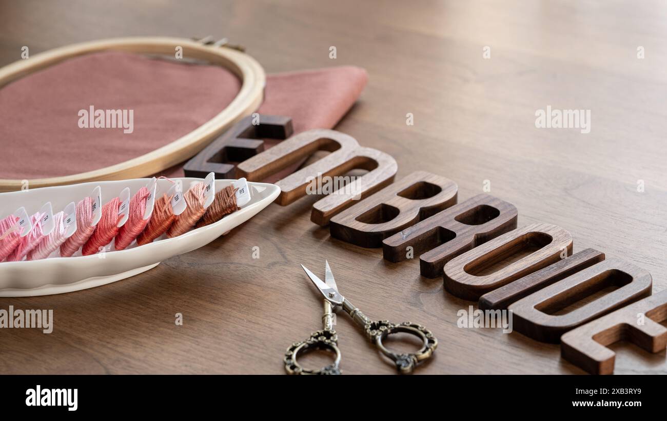 Holzbuchstaben mit Stickerei und Schere auf hölzernem Hintergrund Stockfoto