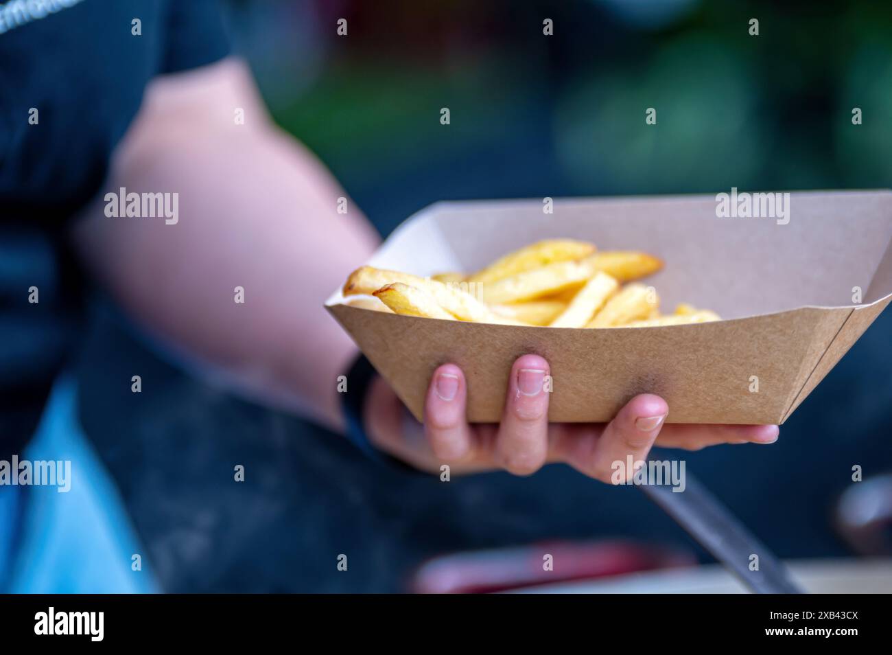 Eine Person hält einen Behälter mit Pommes frites. Hintergrund mit selektivem Fokus und Kopierbereich. Stockfoto