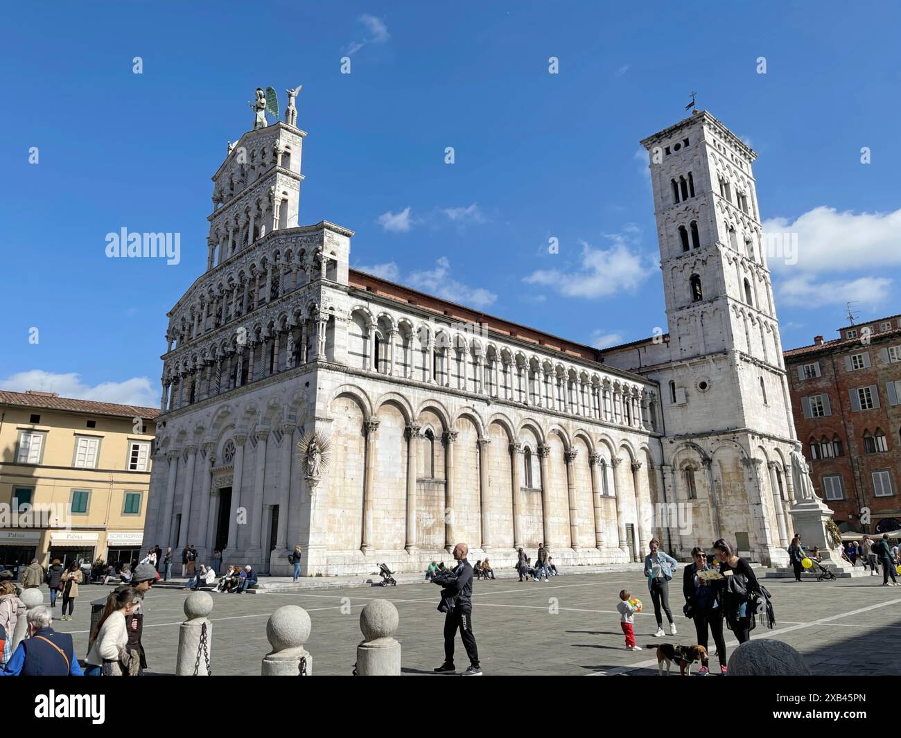 Menschen an sonnigen Tagen auf dem Platz in der Nähe der Kirche San Michele in Lucca, Italien. Tourismus und Attraktionen. März 2023. Stockfoto