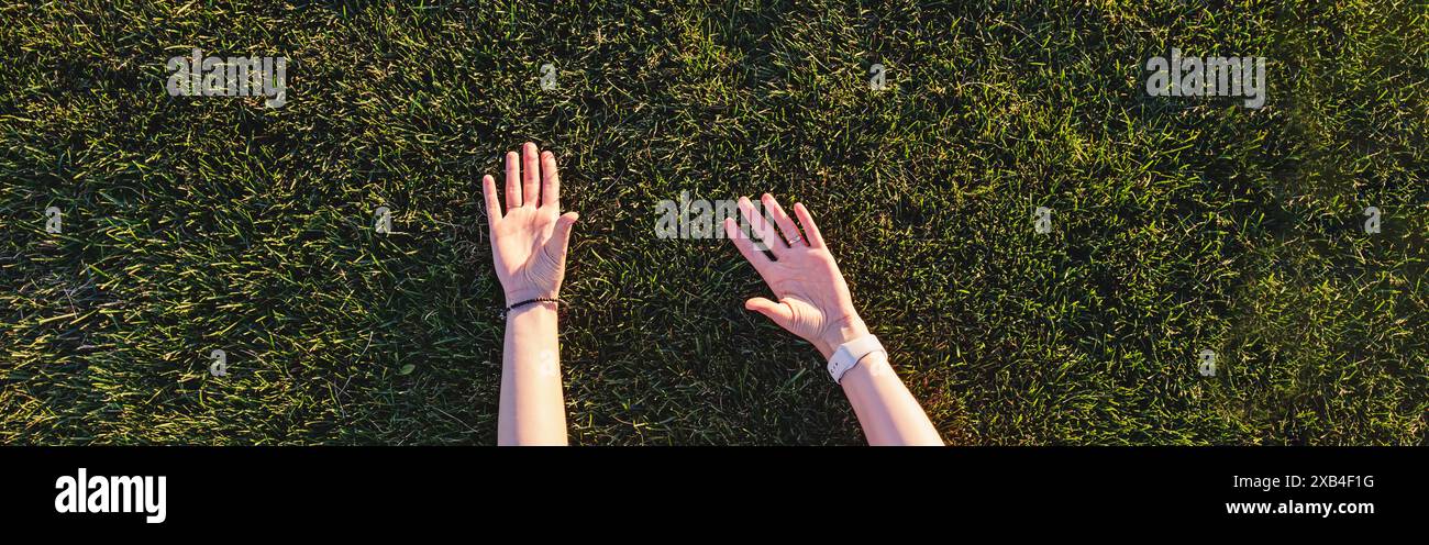 Erhobene Hände der Frau, die auf grünem Gras liegt, natürliches Sonnenlicht, Verbindung zur Natur Stockfoto