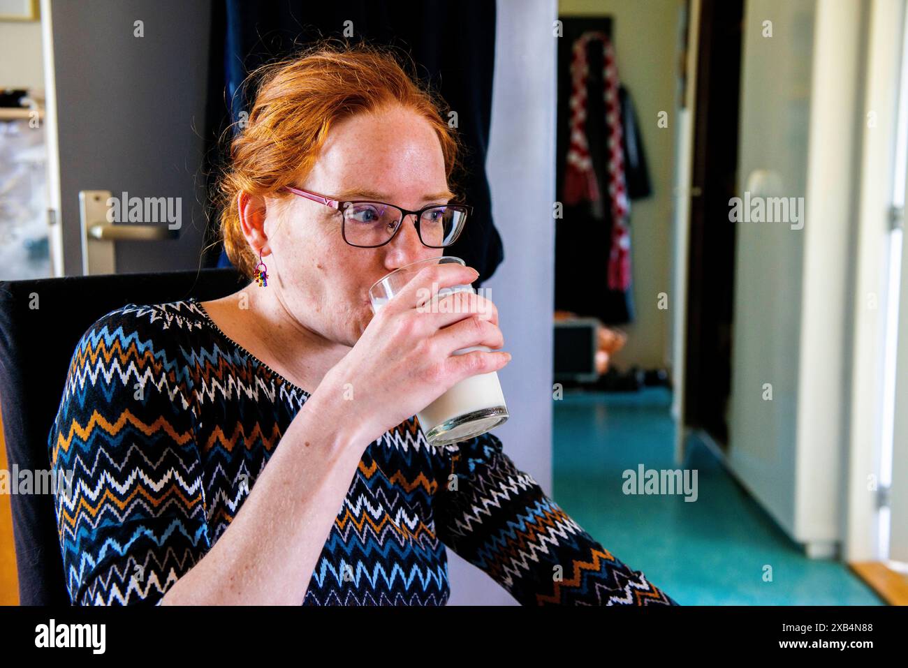 Junge Frau und Glas Milch Junge Frau trinkt ein Glas Milch, während sie an ihrem Esstisch sitzt. Roosendaal, Niederlande. Roosendaal zu Hause in Jan Vermeerlaan Noord-Brabant Nederland Copyright: XGuidoxKoppesxPhotox Stockfoto