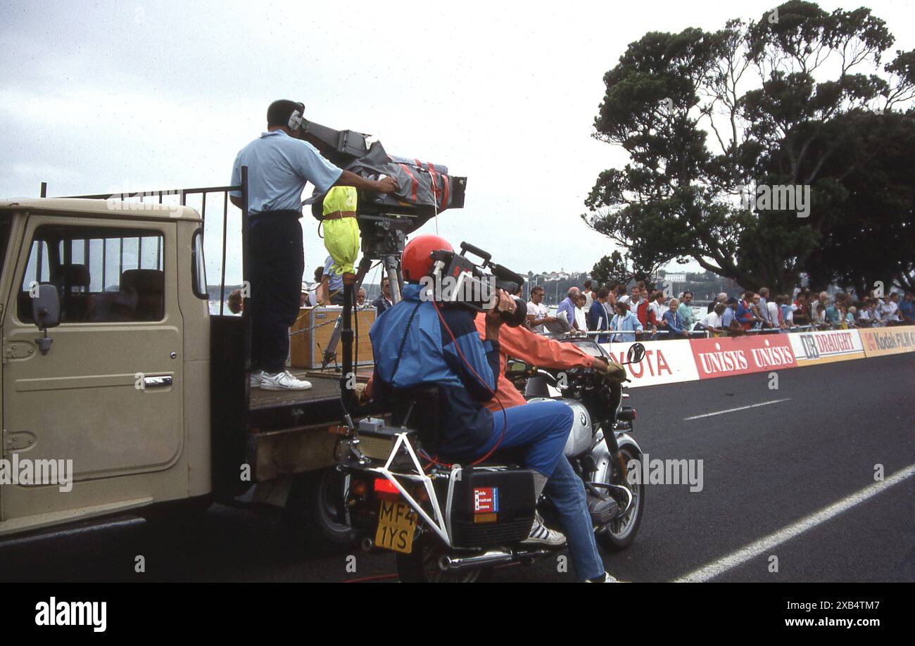 1990, Commonwealth Games, Zuschauer und TV-Kameras, eine auf der hinteren Plattform eines kleinen Lastwagens und eine andere auf einem Motorrad auf der Rennstrecke des Radrennrennens in Auckland, Neuseeland. Die Veranstaltung fand in der Nähe der Avondale-Rennbahn statt und wurde von dem einheimischen Fahrer Graeme Miller gewonnen, der auch eine Goldmedaille im Zeitfahren der Männer gewann. Stockfoto