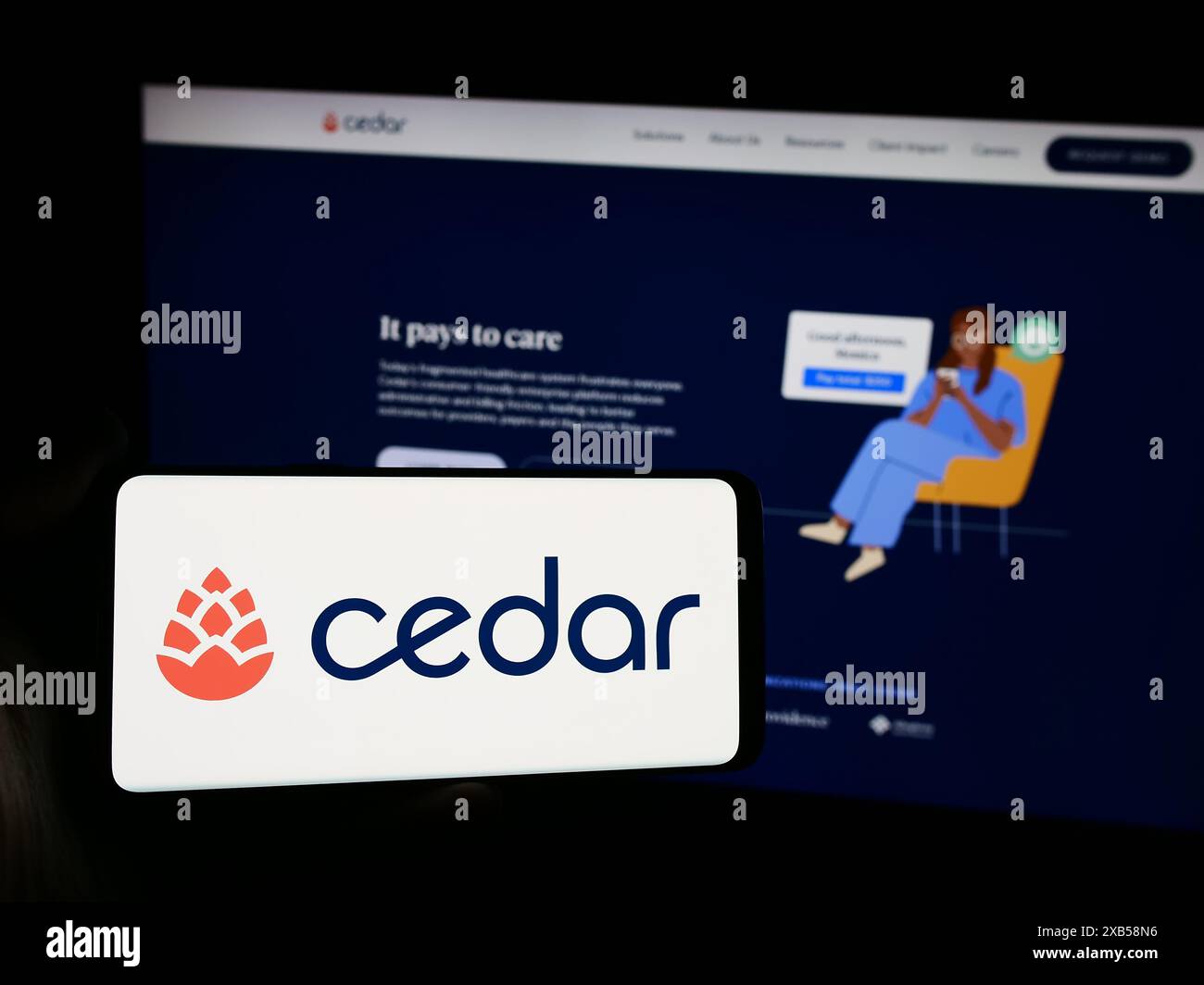 Person mit Smartphone und Logo des US-amerikanischen Softwareunternehmens Cedar Cares Inc. Vor der Website. Schwerpunkt auf dem Display des Telefons. Stockfoto