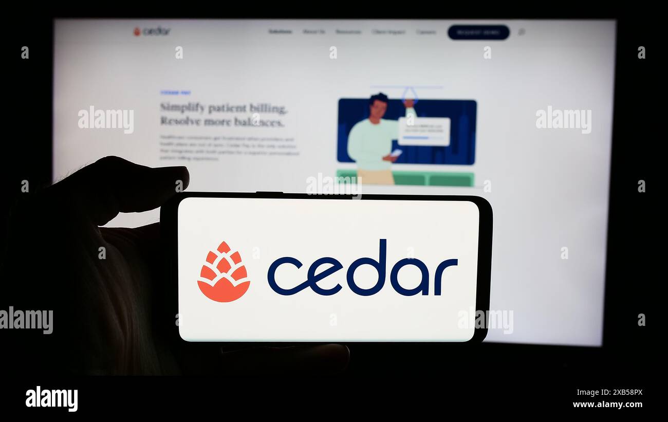 Person, die ein Mobiltelefon mit dem Logo des US-amerikanischen Gesundheitssoftware-Unternehmens Cedar Cares Inc. Vor der Website des Unternehmens hält. Schwerpunkt auf dem Display des Telefons. Stockfoto