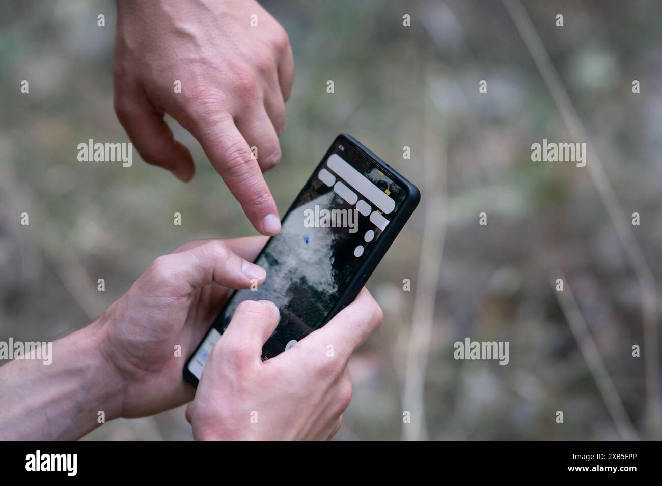 Nahaufnahme eines Mannes, der die gps-Navigations-App auf seinem Smartphone in der Natur verwendet, und eines anderen Mannes, der mit dem Finger auf den Bildschirm zeigt und das Telefon als Navigation verwendet Stockfoto