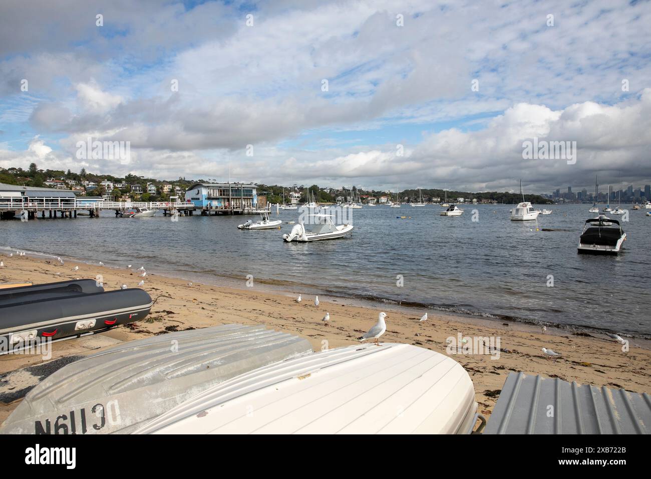 Watsons Bay Beach mit Ruderbootladen am Ufer und Blick über den Hafen zum Stadtzentrum von Sydney und CBD mit Hochhäusern, NSW, Australien Stockfoto