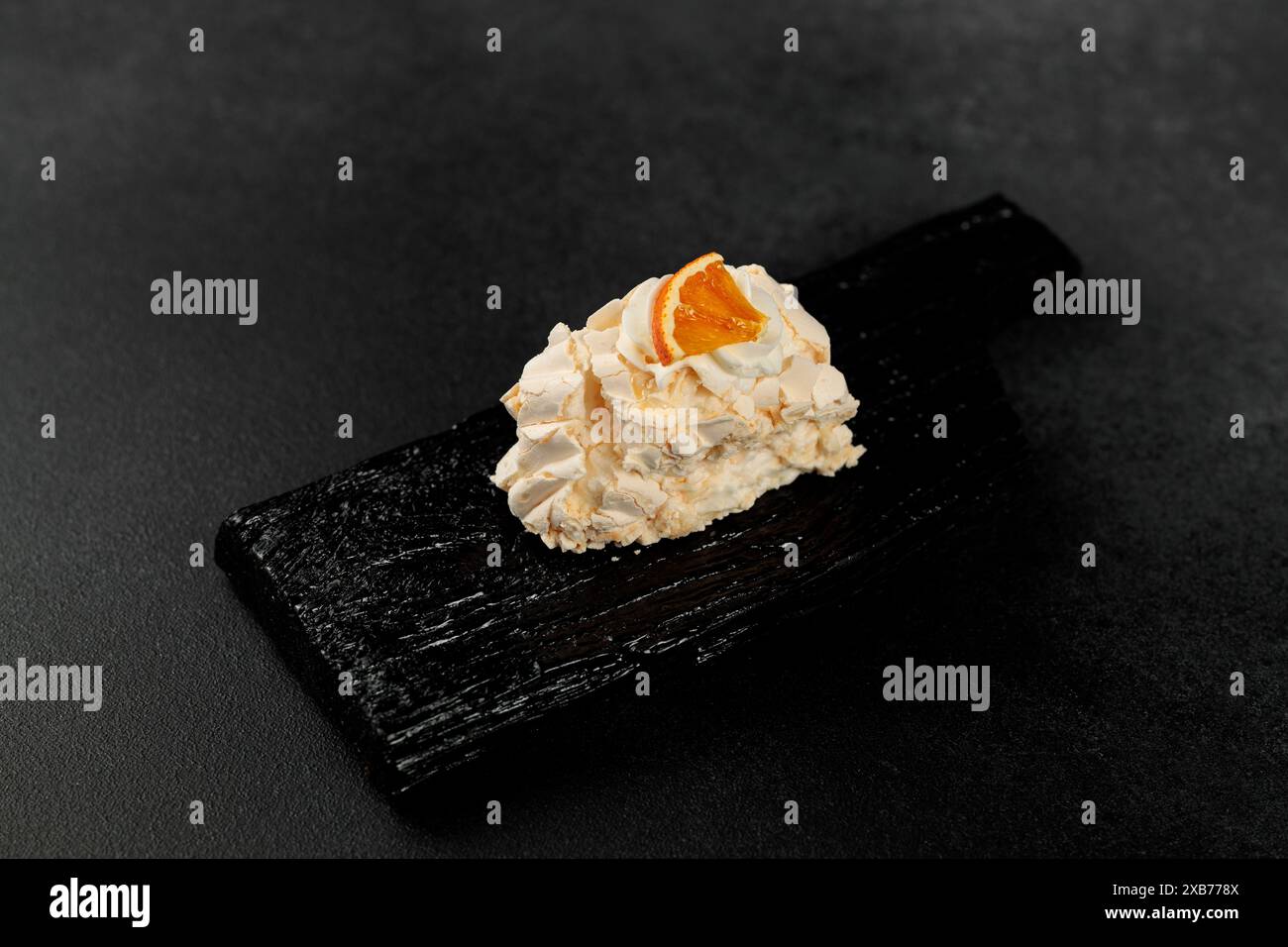 Meringue-Rolle. Geschlagene Proteine und Zucker, Füllung - Frischkäse auf Basis von Weichkäse und Sahne auf einem schwarzen Schneidebrett Stockfoto