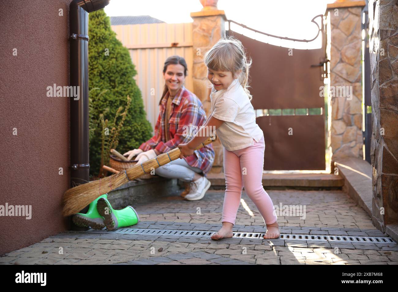 Mutter und ihre süße Tochter putzen zusammen in der Nähe des Hauses am Frühlingstag Stockfoto