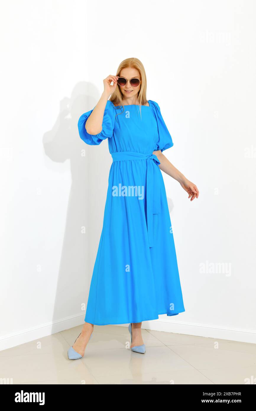 Dynamisches, durchgehendes Porträt einer Frau in einem hellblauen Kleid und passenden Schuhen vor weißem Hintergrund Stockfoto