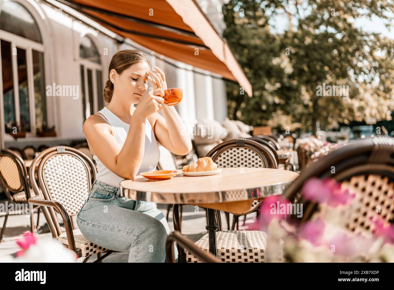 Porträt einer glücklichen Frau, die in einem Café im Freien sitzt und Kaffee trinkt. Frau, die sich im Café am Tisch auf der Straße entspannt, in einem weißen T-Shirt und jea gekleidet Stockfoto